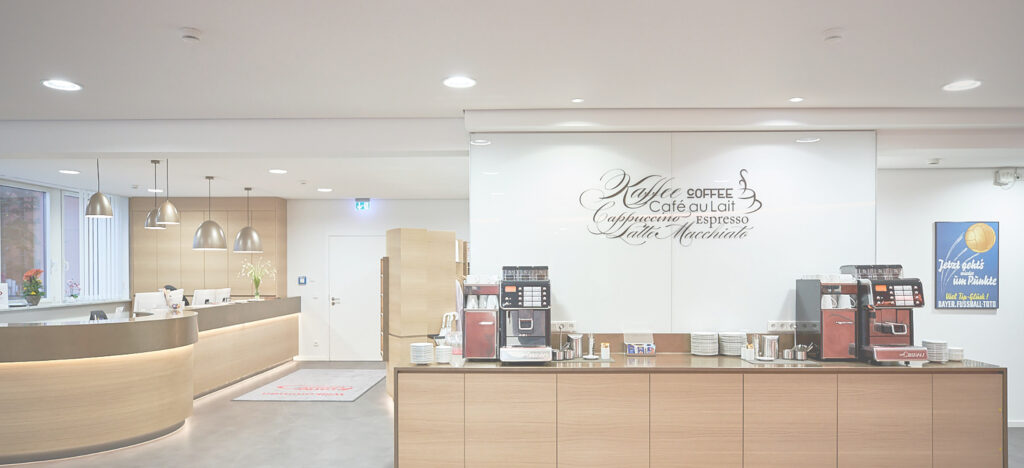 Foto einer modernen, in Holz gehaltenem Empfangsbereich und einer Cafeteria mit Theke, Kaffeemaschinen und stilvoller Beleuchtung.