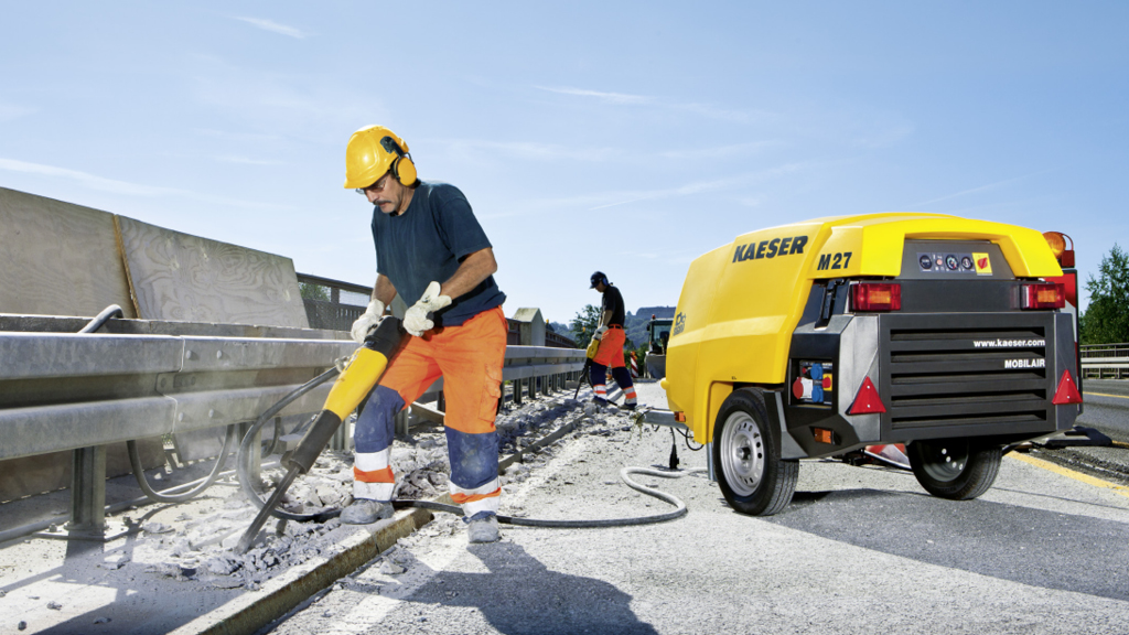 Arbeiter mit Presslufthammer bei Straßenbauarbeiten neben einem gelben Kaeser M27 Kompressor.