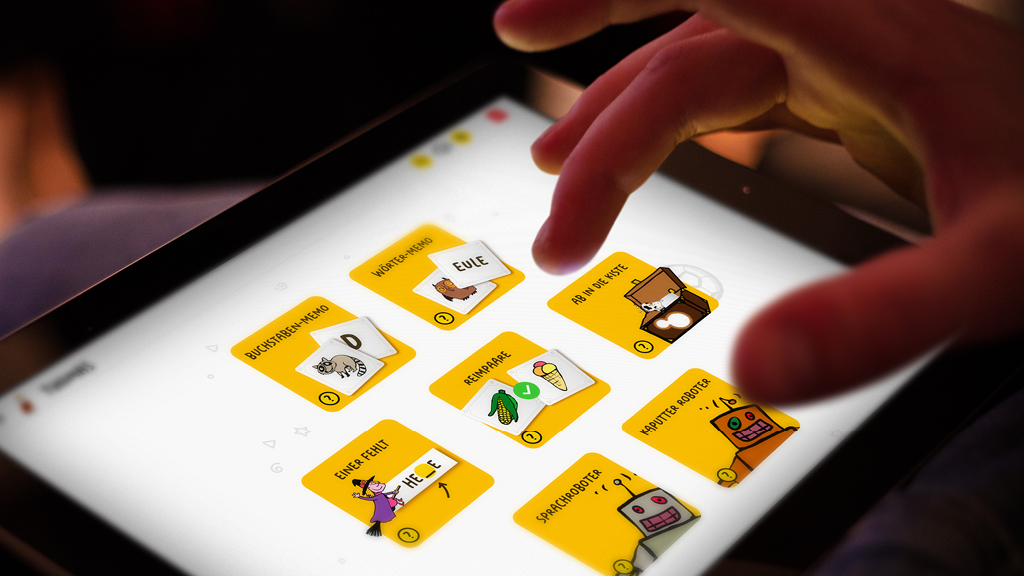 Ein Foto von einem Tabletbildschirm, auf dem verschiedene Spiele angezeigt werden. Eine Kinderhand tippt auf den Bildschirm.