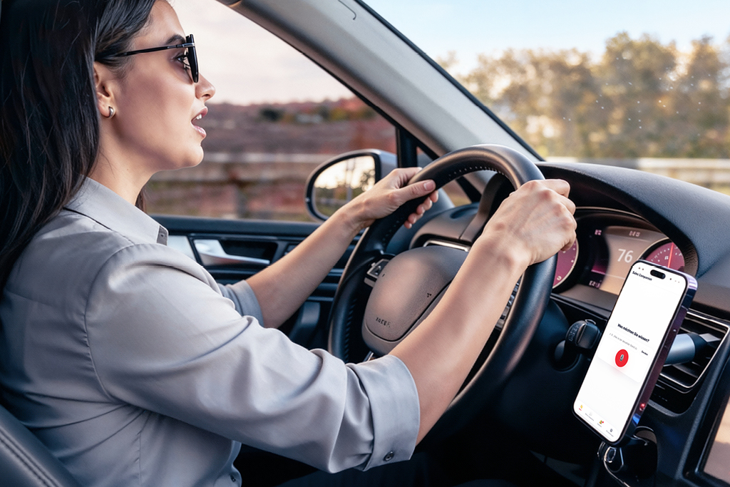 Frau fährt Auto mit Smartphone-Navigation, Hände am Lenkrad, Smartphone am Armaturenbrett befestigt.