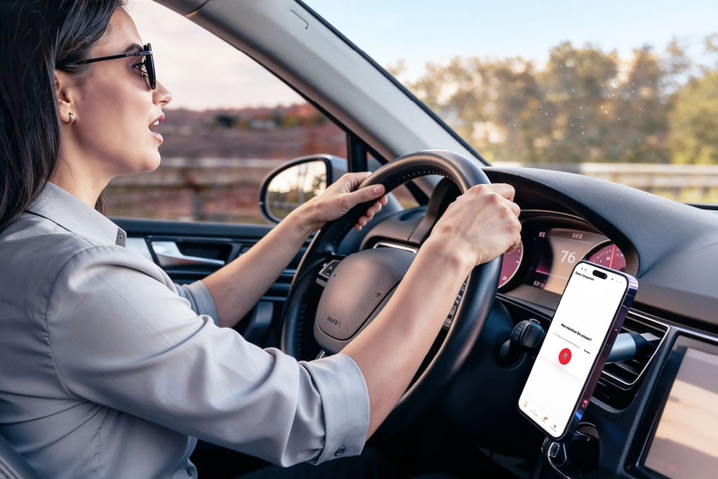 Frau fährt Auto und spricht in ein Smartphone, in dem der Sales Companion Chatbot offen ist.