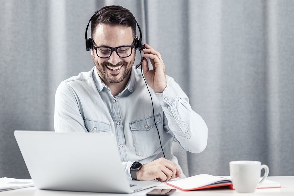 Eine Person mit Headset sitzt vor einem Laptop und telefoniert fröhlich