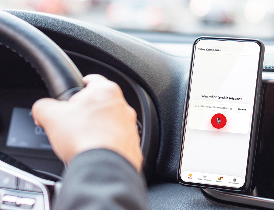 Fahrer nutzt im Auto die Sprachassistenten-Funktion des Sales Companion auf dem Smartphone