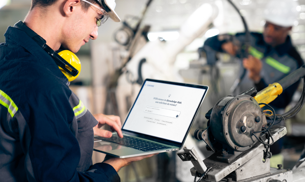 Ein Servicetechniker ruft während der Reparatur eines technischen Geräts Informationen auf einem Laptop ab. Das Bild symbolisiert Lernen im Moment des Bedarfs (Moment of Need).